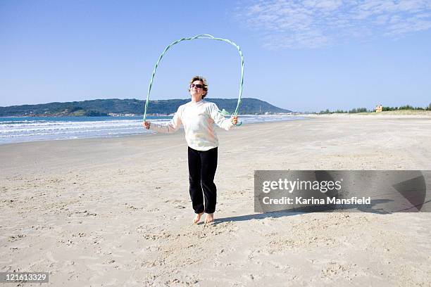 active and happy senior woman skipping at beach - seilspringen stock-fotos und bilder
