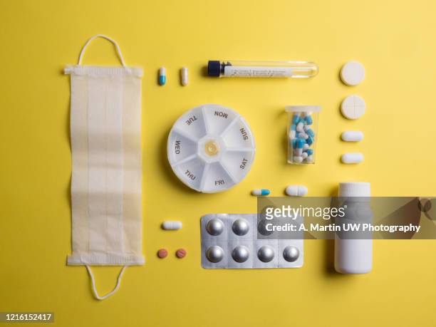 flat layer with various types of pills, capsules, a surgical mask, a test tube and medical supplies on yellow background. - medicamento antiviral imagens e fotografias de stock