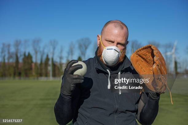 redhead man wearing a face mask and holding baseball equipment at a sports field - amateur baseball stock pictures, royalty-free photos & images