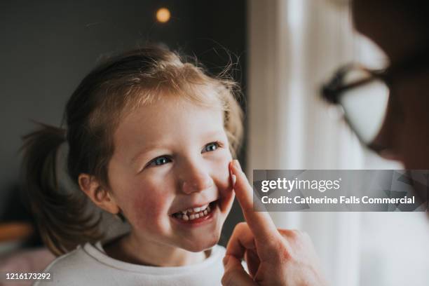 rubbing lotion on cheek - child playing in room stockfoto's en -beelden