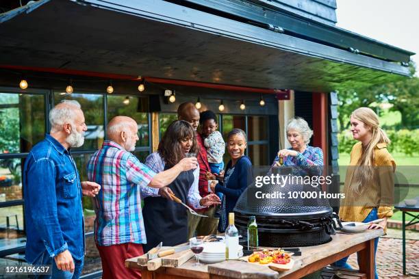 multi generational family standing around barbecue - blended family stockfoto's en -beelden