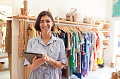 Portrait Of Female Owner Of Fashion Store Checking Stock In Clothing Store With Digital Tablet