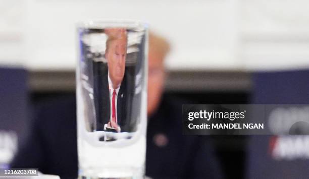 President Donald Trump is seen through a drinking glass as he takes part in a roundtable discussion with industry executives on reopening the...