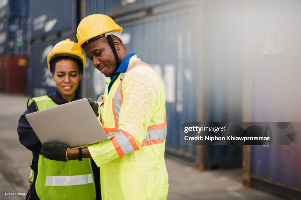 Jonge Afrikaanse Amerikaanse mannen en vrouwenarbeider Controleer en controleer ladingsvracht Containers door computerlaptop bij commercieel scheepvaartdok het kappen gelukkig te gebruiken. Het productexportconcept van vrachtvrachtschepen