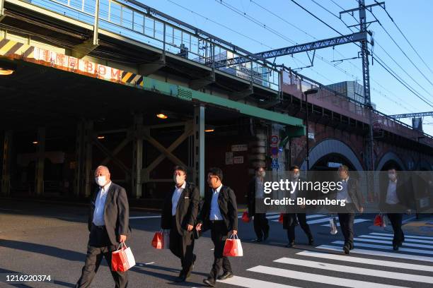 Pedestrians wearing protective masks walk along a street in the Yurakucho district of Tokyo, Japan, Friday on May 29, 2020. Small clusters of...