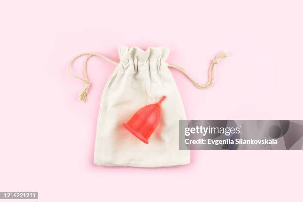 red menstrual cup on cotton bag on pink background. - period cup stockfoto's en -beelden