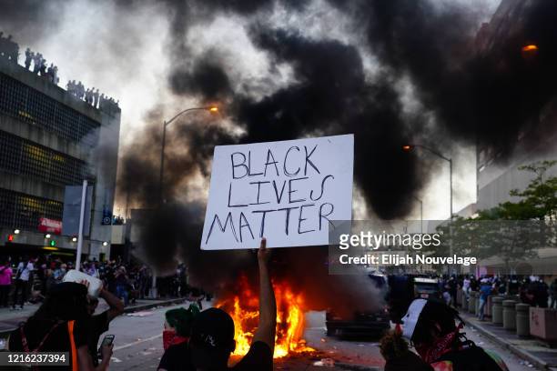 Man holds a Black Lives Matter sign as a police car burns during a protest on May 29, 2020 in Atlanta, Georgia. Demonstrations are being held across...