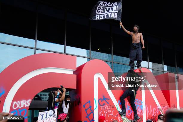 Man waves a Black Lives Matter flag atop the CNN logo during a protest in response to the police killing of George Floyd outside the CNN Center on...