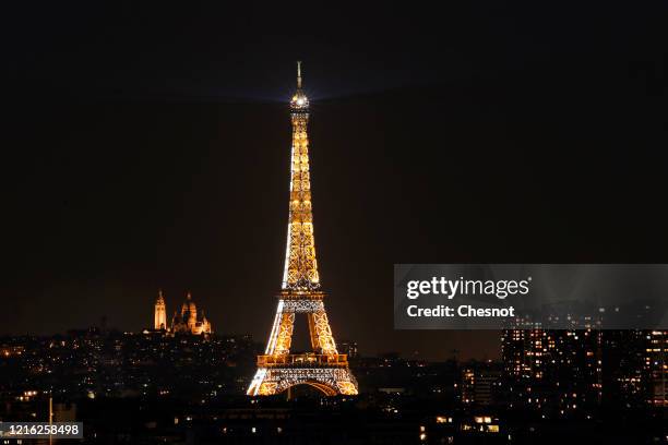 The illuminated Eiffel Tower, the Sacre-Coeur Basilica and the Paris buildings are seen at night while Parisians remain confined to their homes...