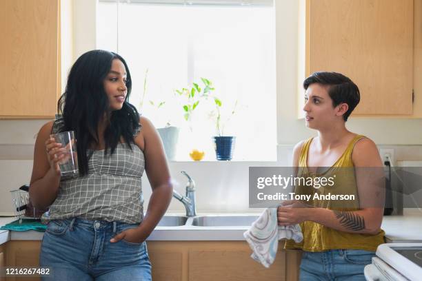 two young women friends talking together in kitchen - two women talking stockfoto's en -beelden