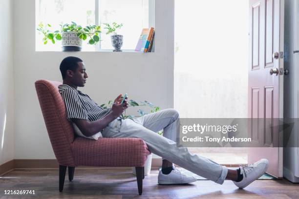 young man with phone sitting in chair in his home - black male profile stockfoto's en -beelden