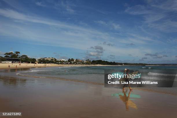 Surfers adhering to new social distancing restrictions head out at Main Beach on March 31, 2020 in Noosa, Australia. Public gatherings are now...
