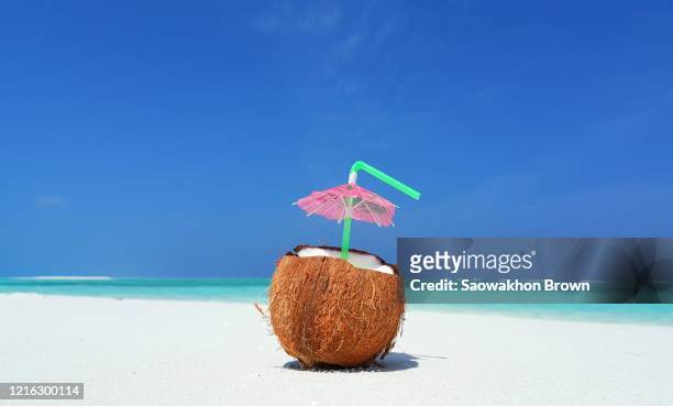 fresh coconut juice on the white sand with blue water and clear sky in the background in maldives - close-up shot - coco fotografías e imágenes de stock
