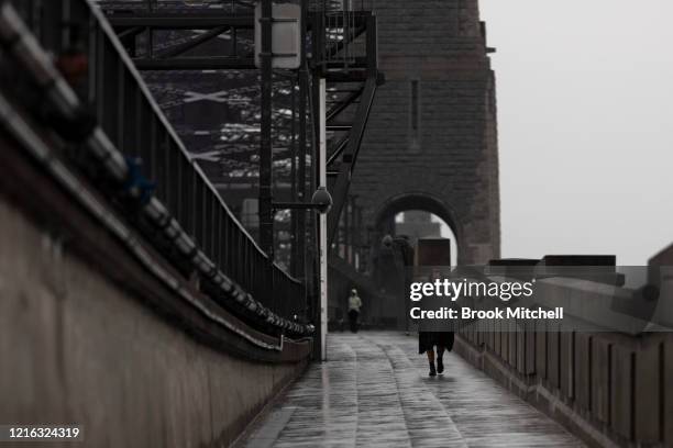 Man walks across the Sydney Harbour Bridge under heavy rain during the partial lockdown on April 02, 2020 in Sydney, Australia. The Australian...