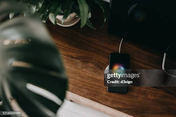 directly above shot of a smartphone getting charged with wireless charging device on a cabinet in the living room - hands free mobile phone stock-fotos und bilder