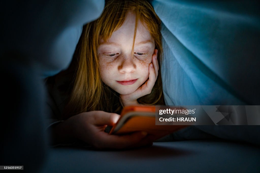 Meisje dat mobiele telefoon in bed in dark gebruikt
