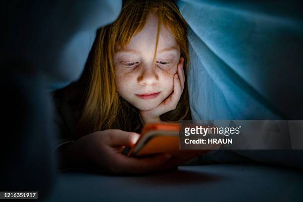 meisje dat mobiele telefoon in bed in dark gebruikt - portable information device stockfoto's en -beelden