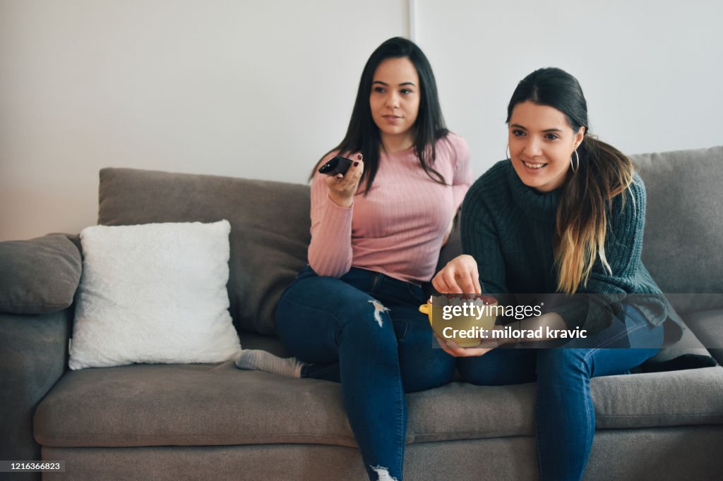 Two women relaxing on sofa in the living room and watching a movie