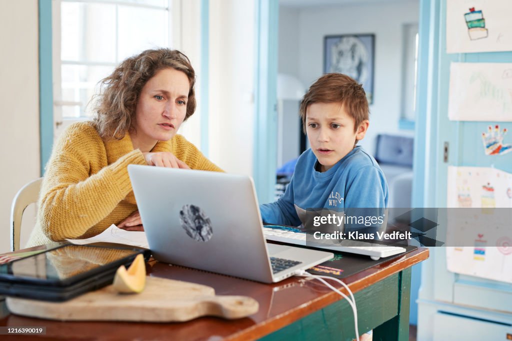 Mother homeschooling son at laptop