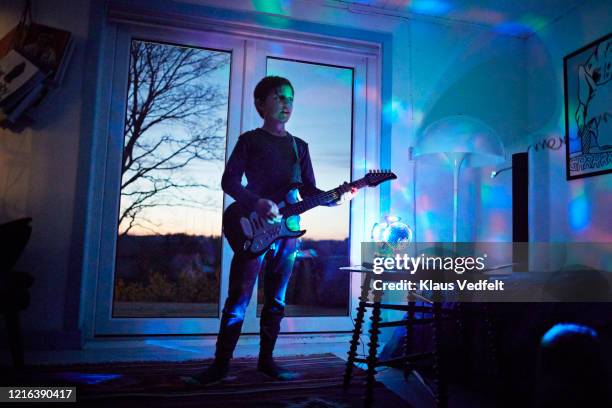 boy playing electric guitar in living room with neon light - puntear un instrumento fotografías e imágenes de stock