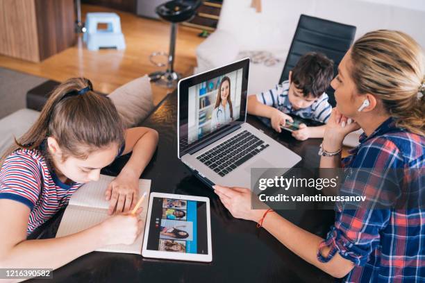 moeder die met arts op laptop probeert te spreken terwijl het letten op twee jonge geitjes die thuis blijven homeschooling en afstandsleren - family technology stockfoto's en -beelden