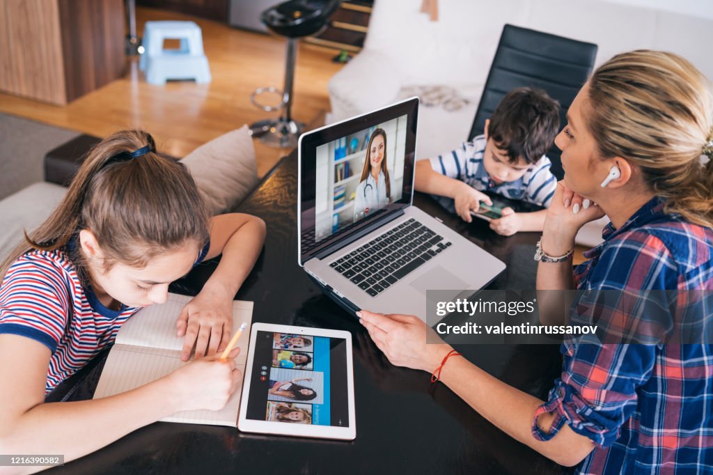 Mother trying to talk with doctor on laptop while watching two kids staying home Homeschooling and distance learning