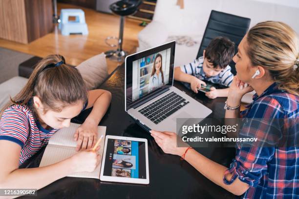mother trying to talk with doctor on laptop while watching two kids staying home homeschooling and distance learning - woman home with sick children imagens e fotografias de stock