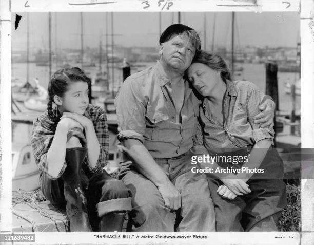 Actors Wallace Beery and Marjorie Main sitting at a dock with child actress Virginia Weidler in a scene from the film 'Barnacle Bill', 1941.