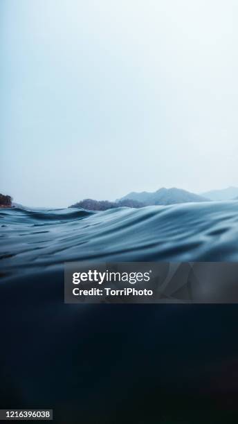 a split level of above and below the lake surface in deep blue water off the lakeshore wirh hills - wateroppervlak stockfoto's en -beelden