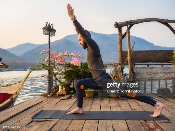 warrior pose on the lake. morning outdoors mens yoga - man doing yoga in the morning stockfoto's en -beelden