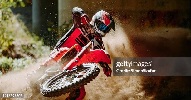 le pilote de motocross dans le sportswear rouge a couru sur la piste de saleté dans la forêt - motocross stock photos et images de collection