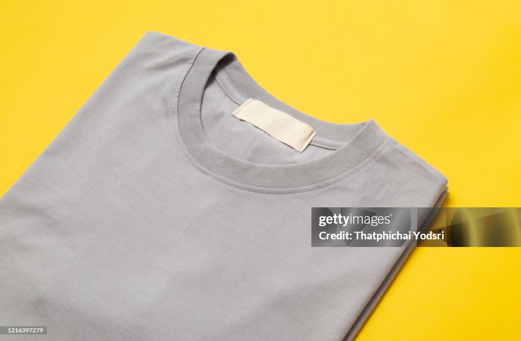 灰色摺疊T恤與空白標籤,為您的設計隔離在黃色背景
