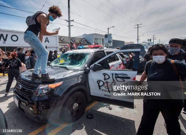 Demonstrators stand on a smashed police vehicle in the Fairfax District as they protest the death of George Floyd, in Los Angeles, California on May...