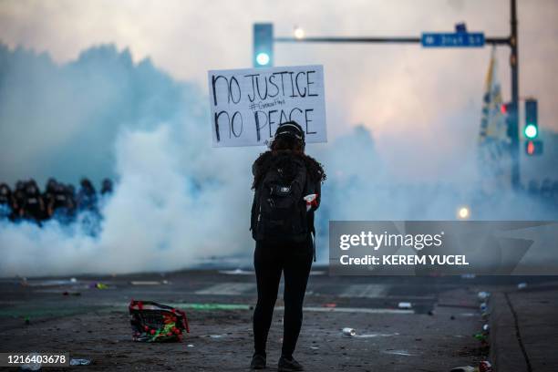 Smoke rises near a demonstrator holding a sign and facing a row of police near the 5th police precinct during a demonstration to call for justice for...