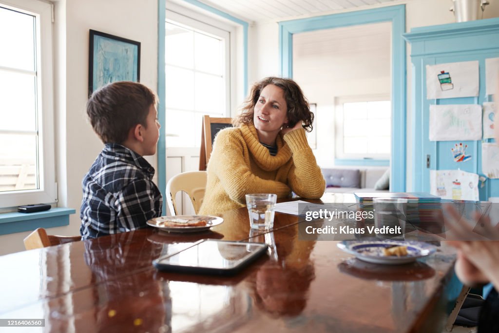Mother and son eating and doing homework at dining table
