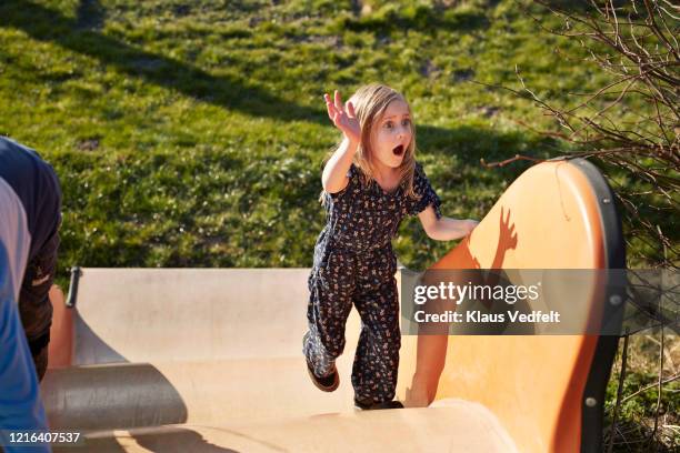 surprised girl climbing sunny playground slide - rutsche stock-fotos und bilder