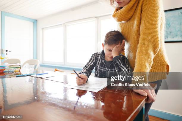 mother watching frustrated son doing homework at dining table - homework frustration stock pictures, royalty-free photos & images