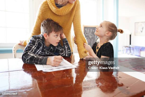 mother homeschooling daughter and son at dining table - exigir - fotografias e filmes do acervo