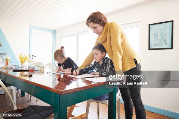 mother homeschooling daughter and son at dining table - educación en el hogar fotografías e imágenes de stock