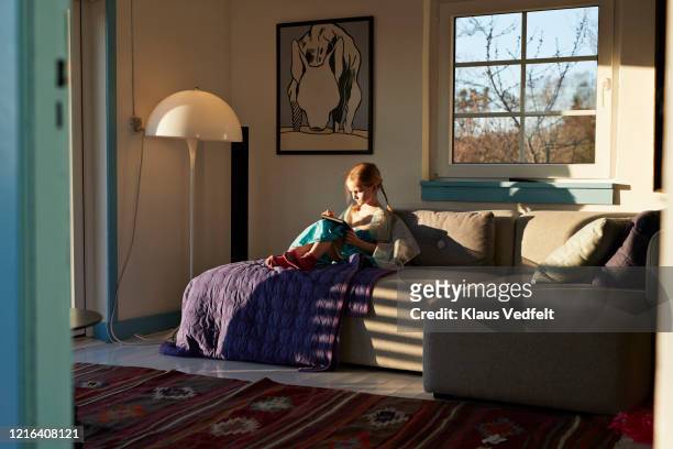 girl using digital tablet on sunny living room sofa - game one stockfoto's en -beelden