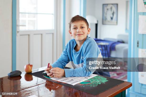 portrait smiling boy doing homework at dining table - sitting at table looking at camera stock-fotos und bilder