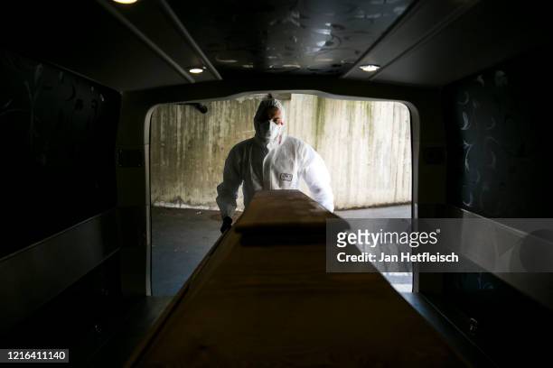 Undertaker worker Leon dressed in full protective clothing and mask pushes a coffin carrying a deceased Covid-19 victim into a mortuary van at a...