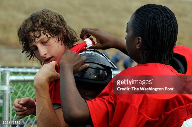 Players trying out for the Patriot Football Team put on shoulder pads before morning practice on August 9, 2011. Marshall Well gets help from Robert...