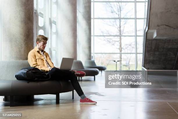 male student sits in comfortable chair to work on laptop - community college campus stock pictures, royalty-free photos & images