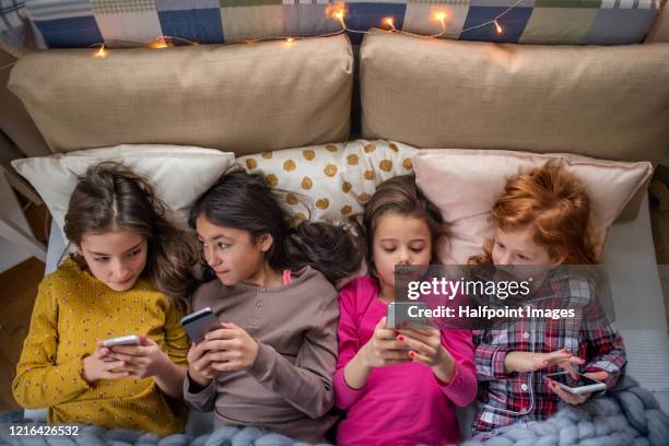 view from above of group of small girl friends on bed, using their phones. - alpha stock pictures, royalty-free photos & images