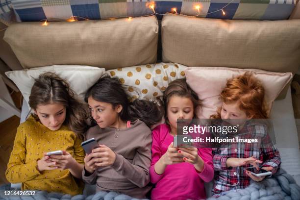 view from above of group of small girl friends on bed, using their phones. - slumber party - fotografias e filmes do acervo