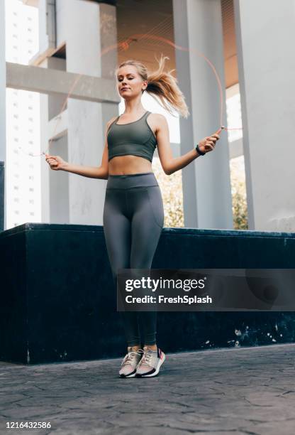 cardio-übung: schöne blonde frau in fitness strumpfhosen und top jumping the rope - seilspringen stock-fotos und bilder