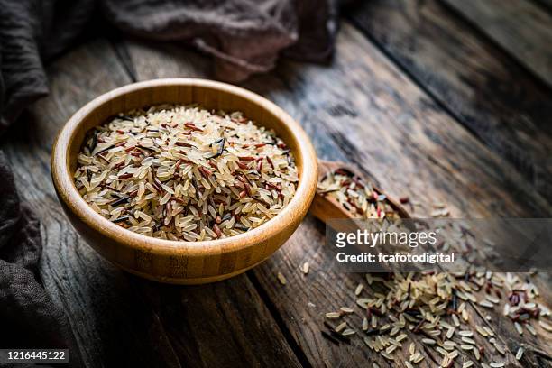 cuenco de madera relleno con arroz mezclado rodado en la mesa de cocina rústica - arroz integral fotografías e imágenes de stock