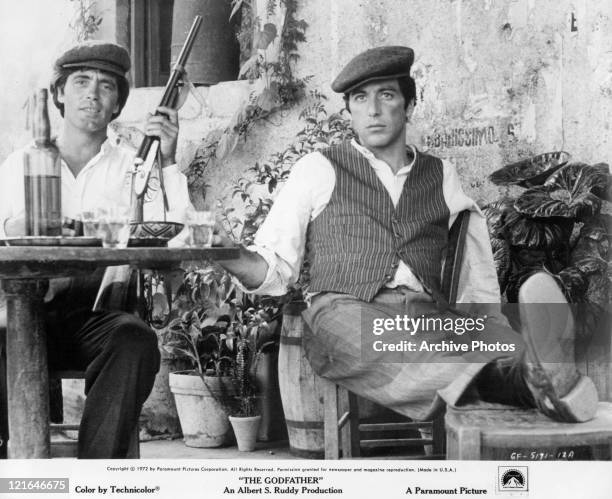 Al Pacino sits at a table with an unknown actor that has a gun in his hand in a scene from the film 'The Godfather', 1972.