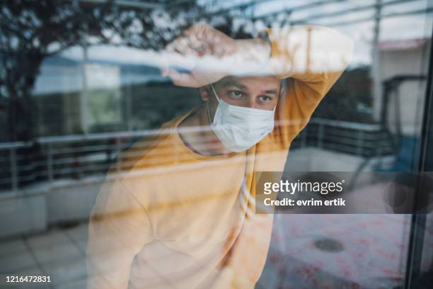 mann in quarantäne trägt eine maske und schaut durch das fenster - quarantäne stock-fotos und bilder